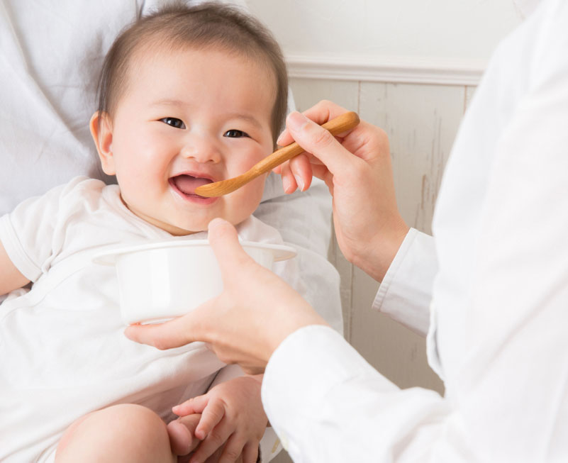 スプーンで離乳食を食べさせられている赤ちゃん