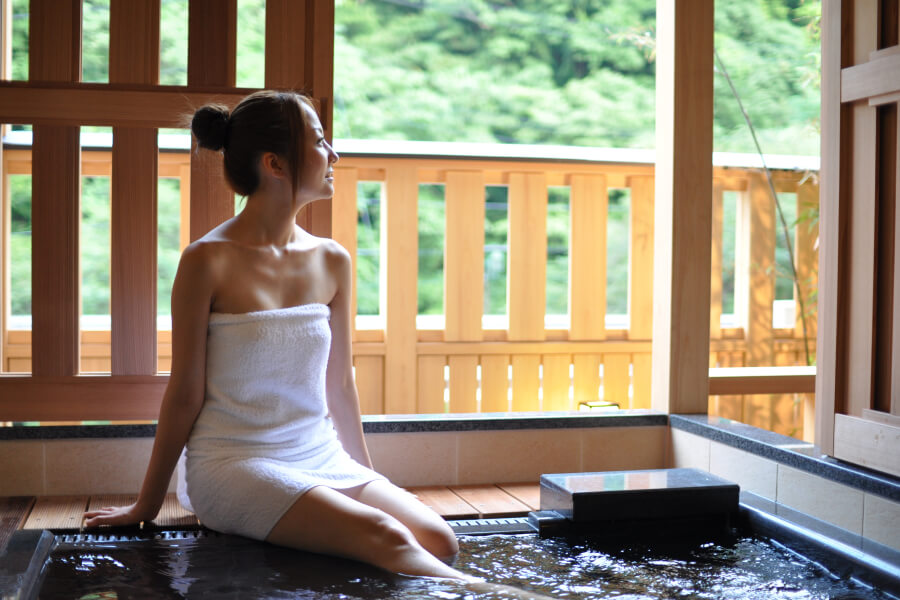 お部屋内の屋根付の露天風呂に足を入れ景色を眺める女性