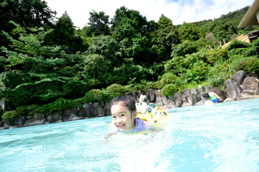 水着で浮き輪を使って屋外プールで泳ぐ女の子。