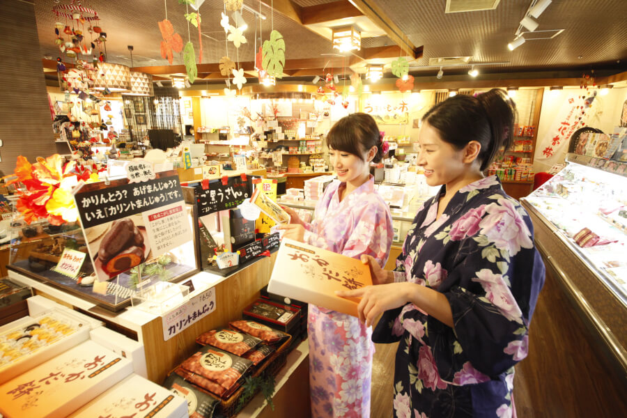 売店でお菓子やおまんじゅう等のお土産を見ている浴衣姿の女性2人。