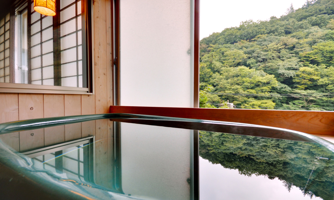 木の縁の浴槽には、外の山々の緑が美しく映り込み、静かな雰囲気が漂っています。