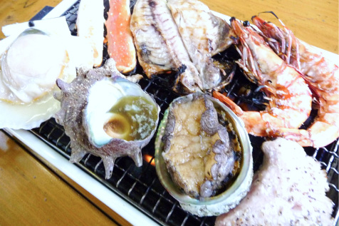 焼き網の上で調理される新鮮な魚介類、エビや貝、アワビなどの豪華な盛り合わせ